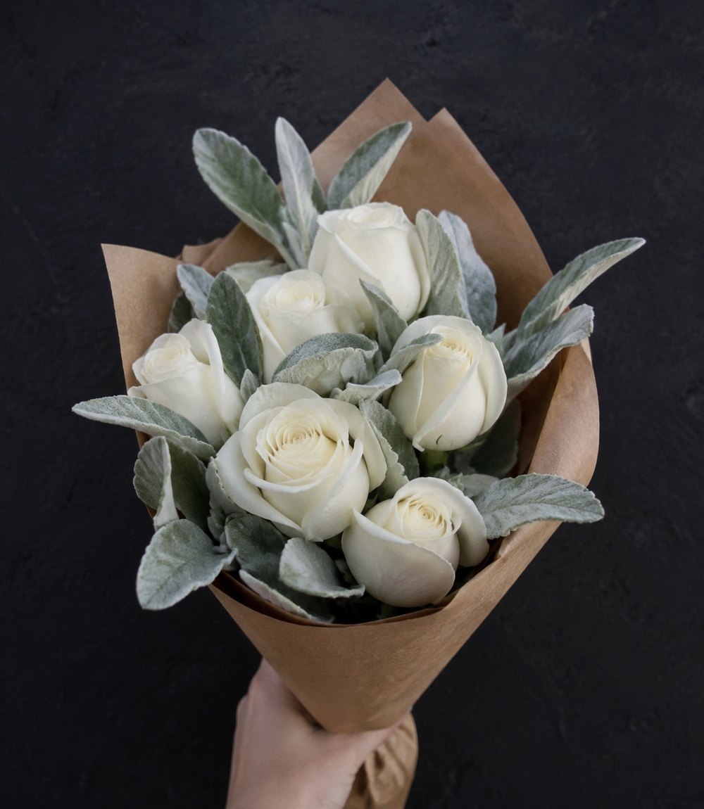 Kleiner Strauß aus weißen Rosen in Packpapier, in einer Hand